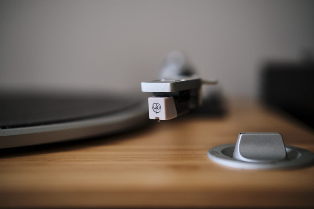 Gros plan sur la cellule et le bras de lecture d'un tourne-disque vintage en bois, avec le plateau flou en arrière-plan.